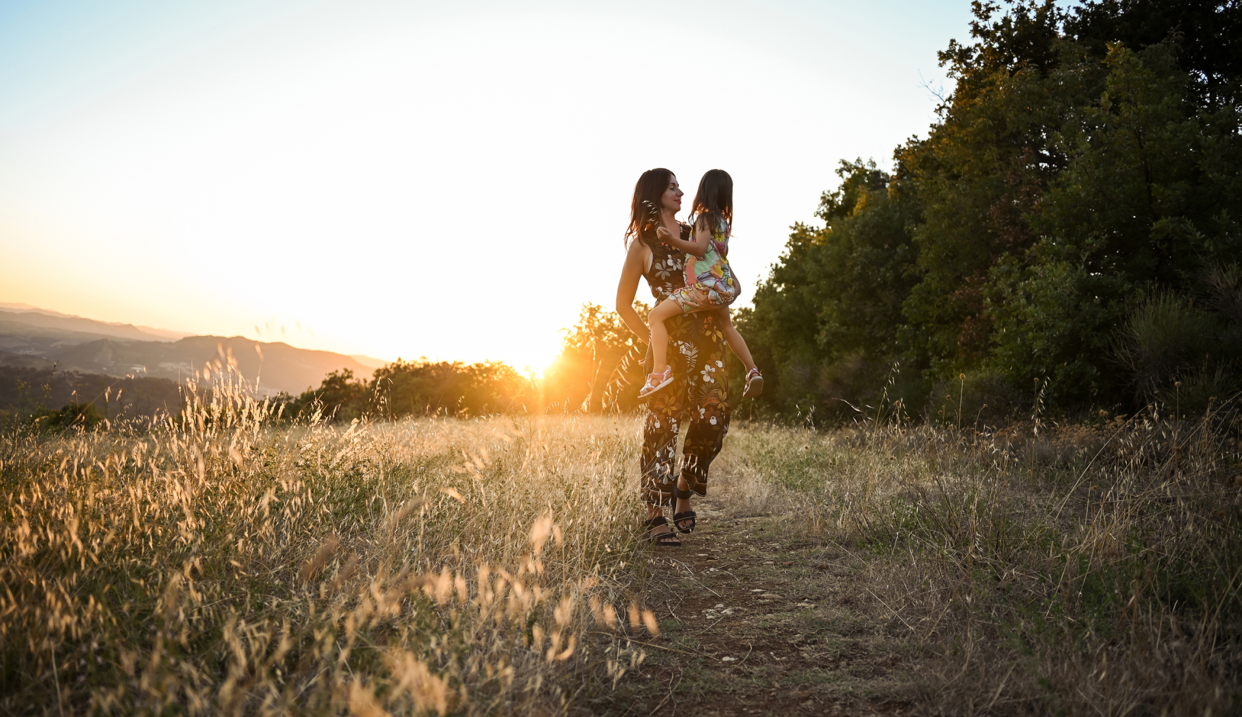 A photo of a woman carrying a young girl in a field of dried grass.